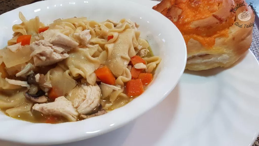 Instant pot chicken noodle soup with a garlic cheese bun on a white plate
