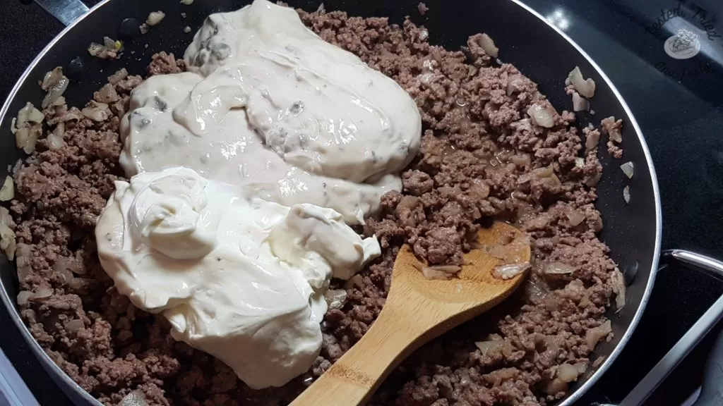 mushroom soup and sour cream being added to extra lean ground beef and onions in a frying pan.