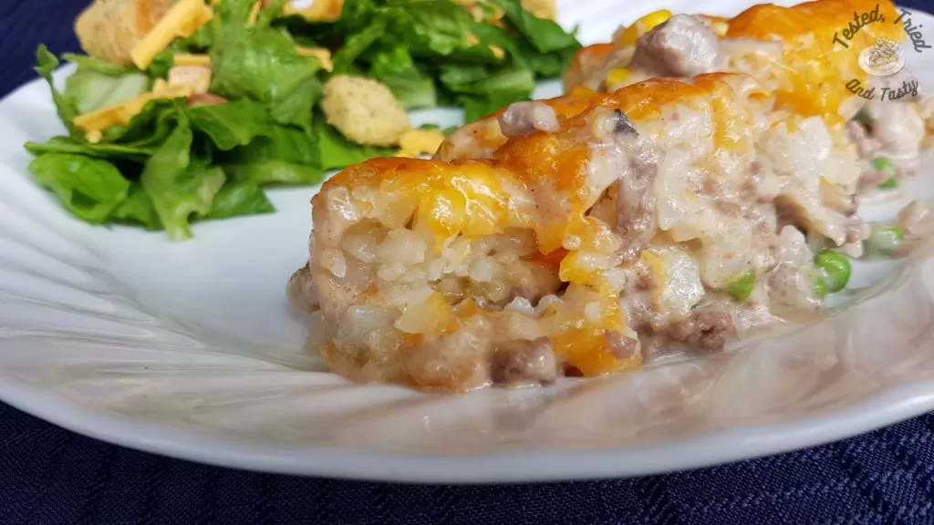 deluxe tater tot casserole with salad on a white plate on a blue tablecloth