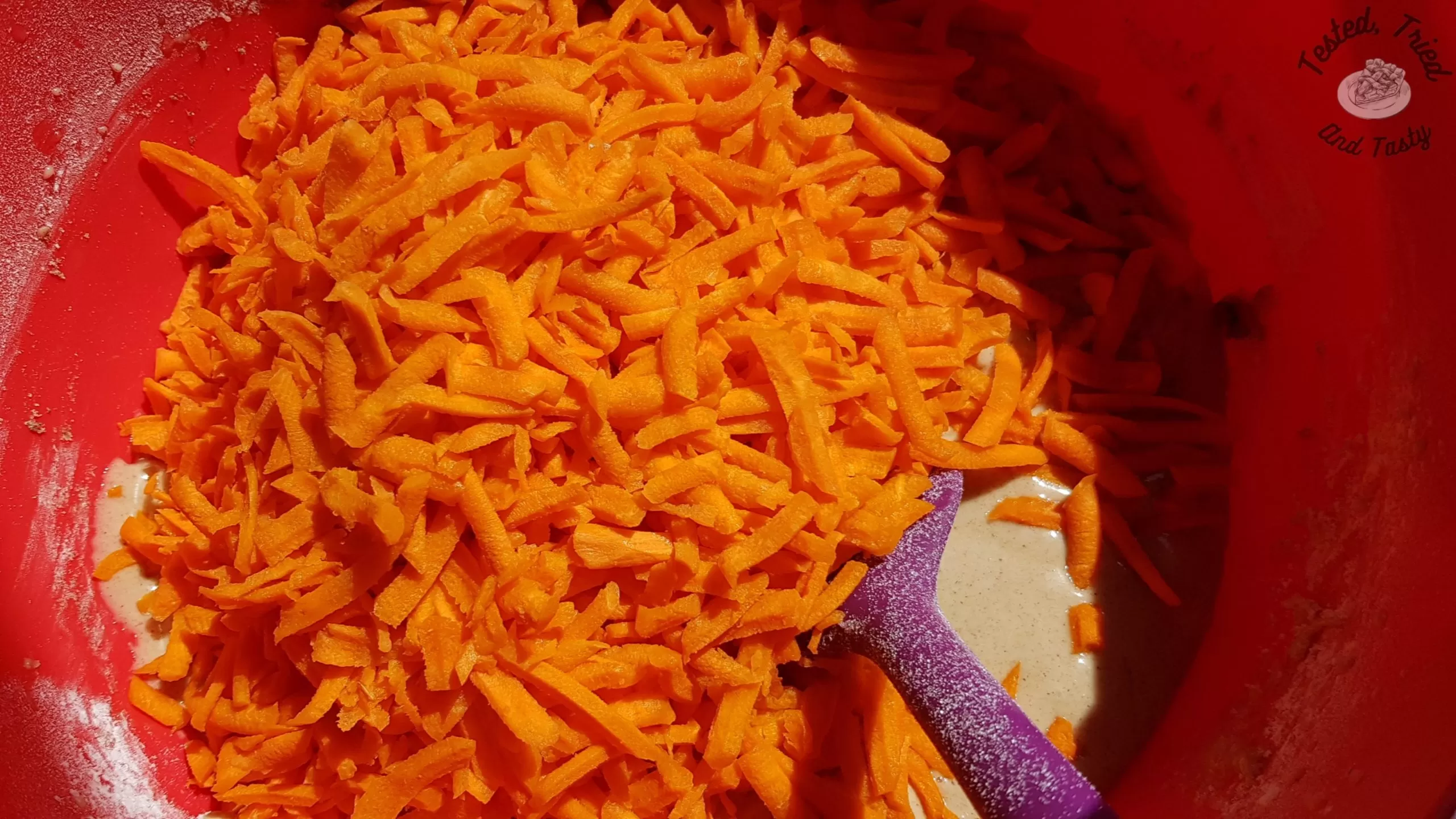 grated carrots added to batter for carrot cake in a red bowl
