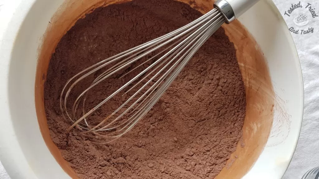 dry ingredients for chocolate cupcakes being whisked in a white bowl,