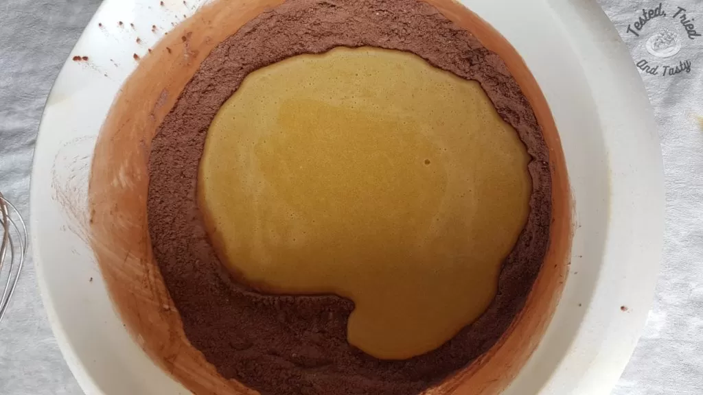 liquid and dry ingredients being mixed for chocolate cupcakes in a white bowl.