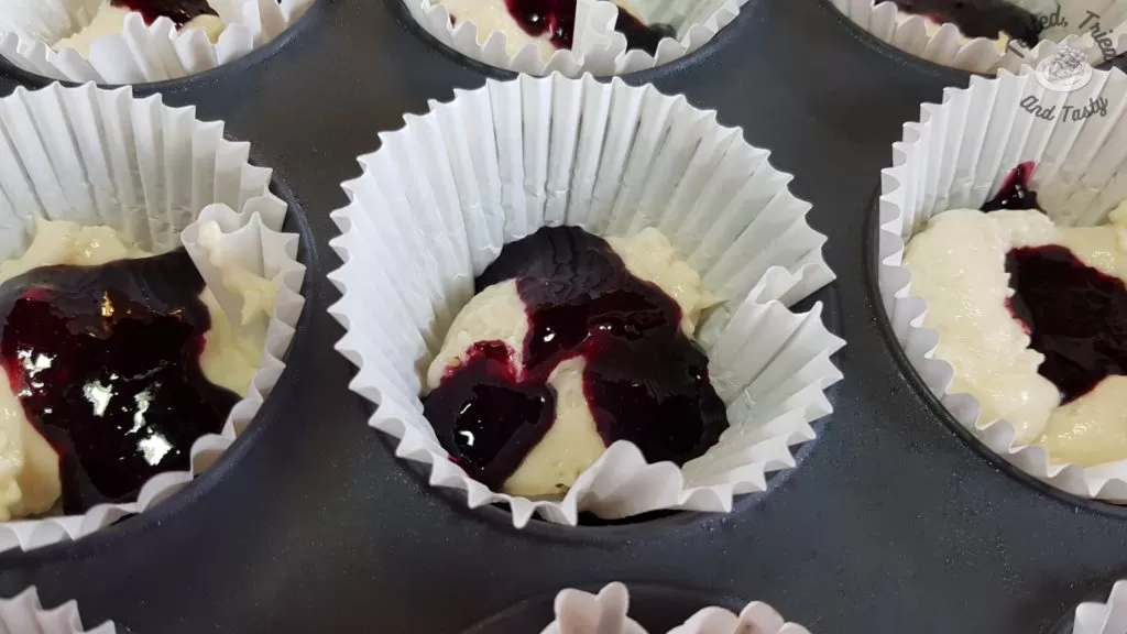 vanilla batter with blueberry syrup in a muffin tin