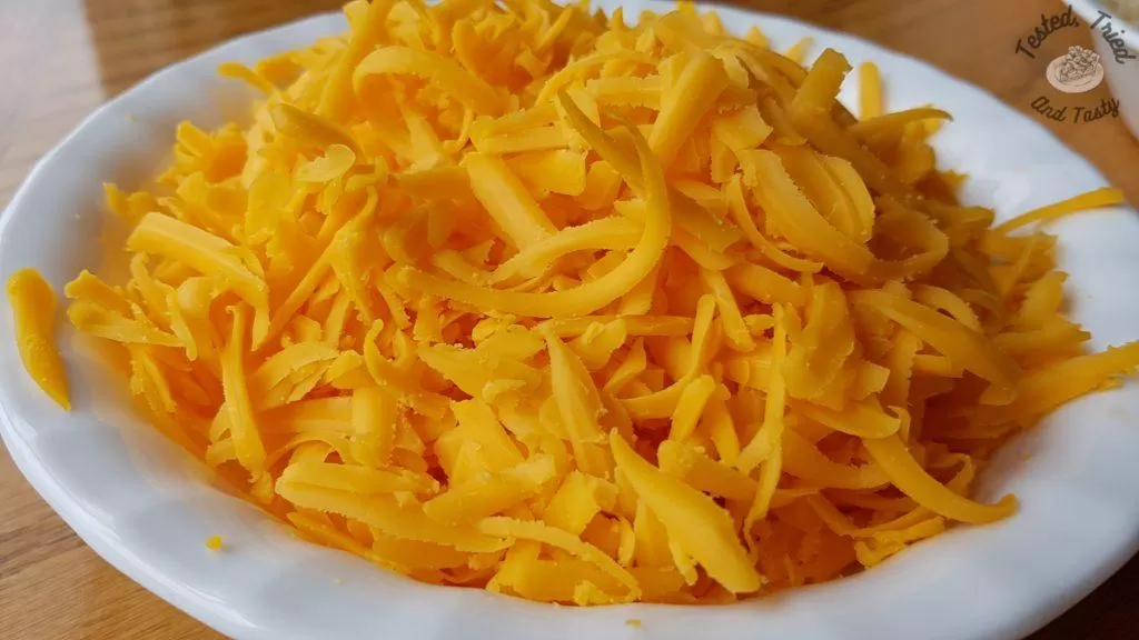 Grated cheddar cheese in a white bowl on a wooden table.