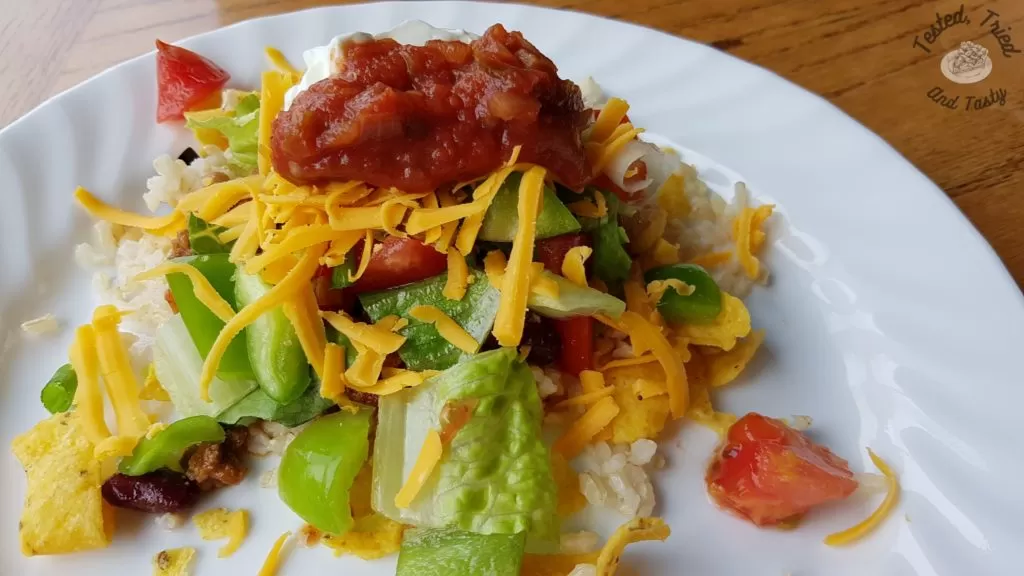 Assembled chili stacker aka haystack on a white plate on a wooden table.
