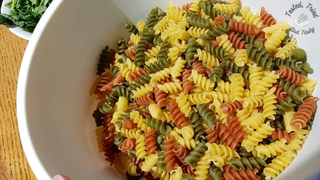 Tri color Rotini in a white bowl on a wooden table.