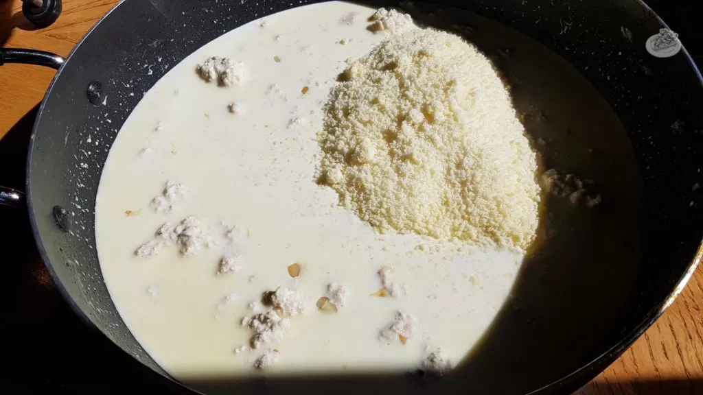 Parmesan cheese added to alfredo sauce in a saucepan.