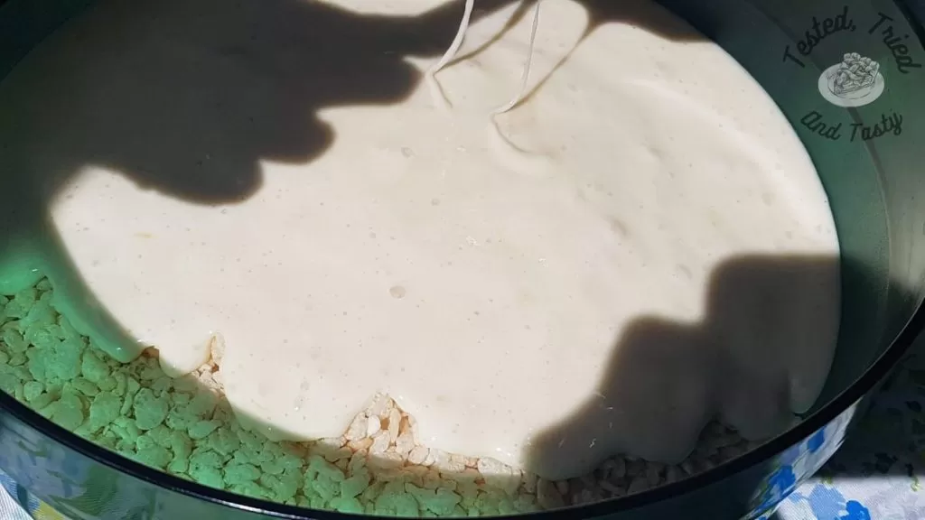 pouring the melted marshmallow mixture onto the rice krispies in a green bowl.