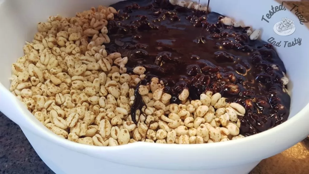 Chocolate syrup on puffed wheat cereal in a large white plastic bowl.