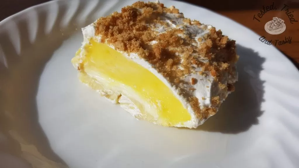 Lemon Lush Pudding dessert on a white plate on a wooden table.