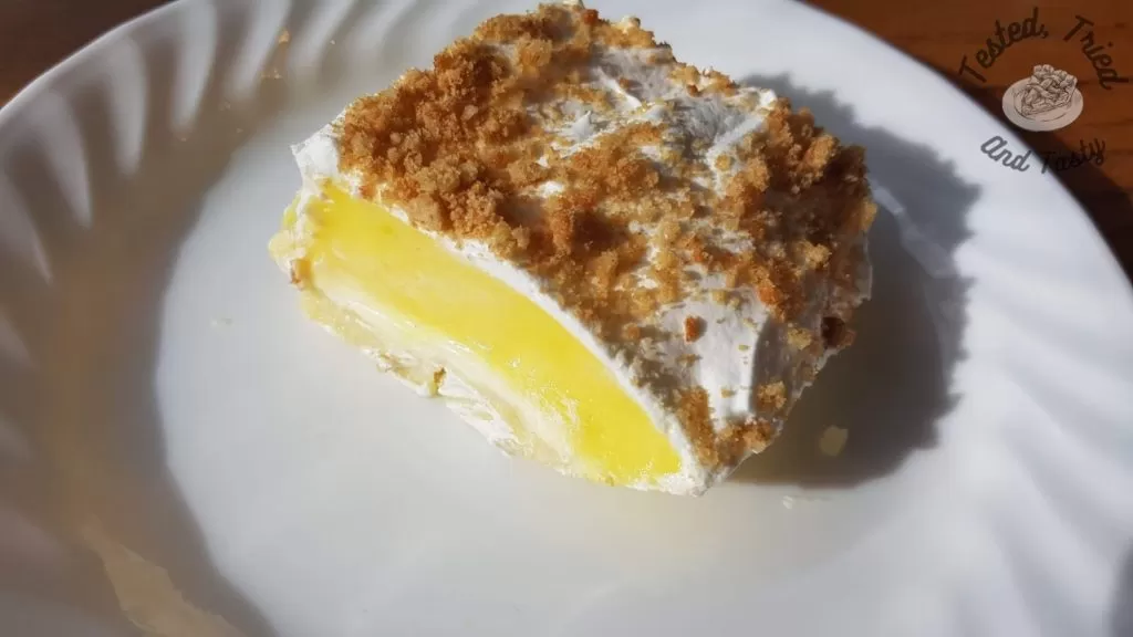 Lemon Lush Pudding Dessert on a white plate on a wooden table.