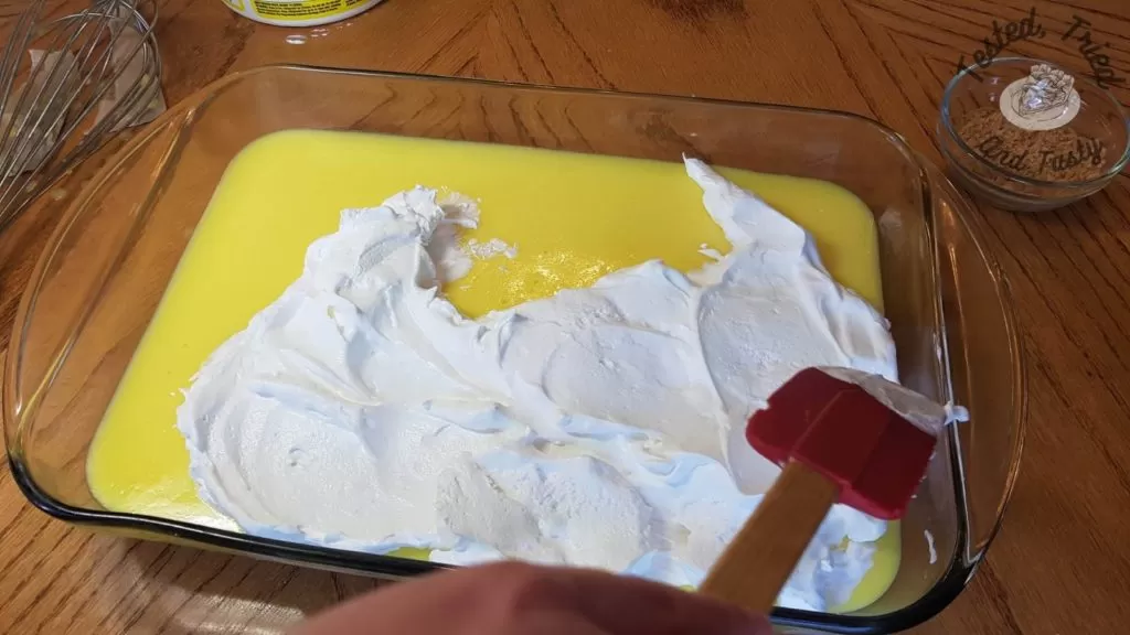 Spreading cool whip onto Lemon Lush Pudding Dessert.