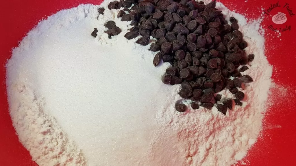 Flour, sugar, baking powder, salt and semi sweet chocolate chips in a red bowl.