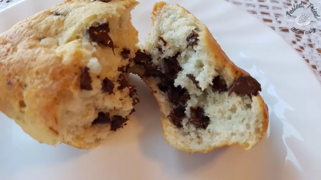 Close up of a banana chocolate chip muffin on a white plate on a lace tablecloth.