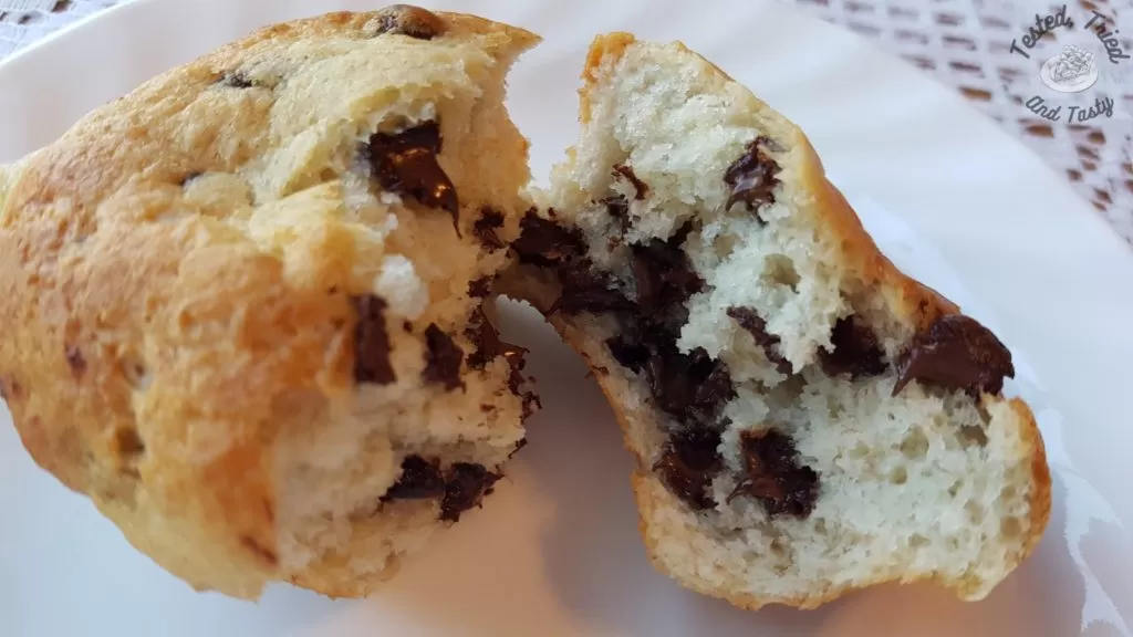 Close up of a banana chocolate chip muffin on a white plate on a lace tablecloth.