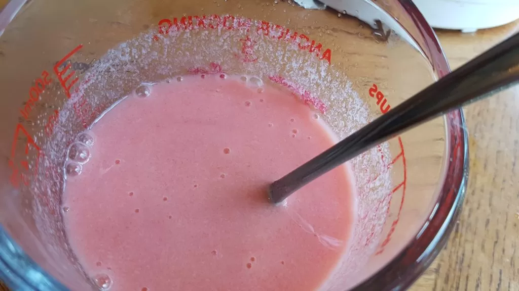 Peach jello mixed with water and evaporated milk in a glass measuring cup.