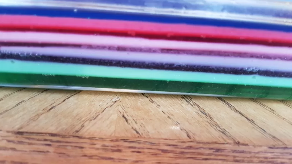 Layered Rainbow jello recipe in a glass dish on a wooden table.