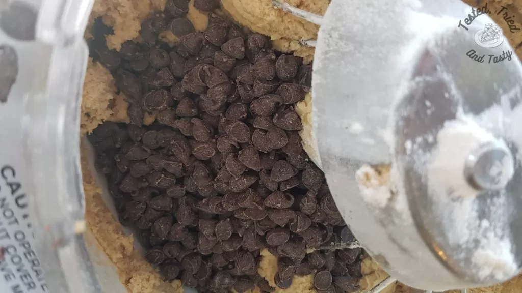 Chocolate chips added to cookie batter in a bosch mixer.