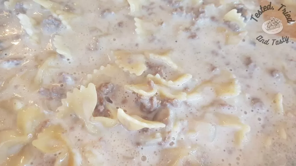 Pasta added to ground beef and mushrooms in a large skillet.