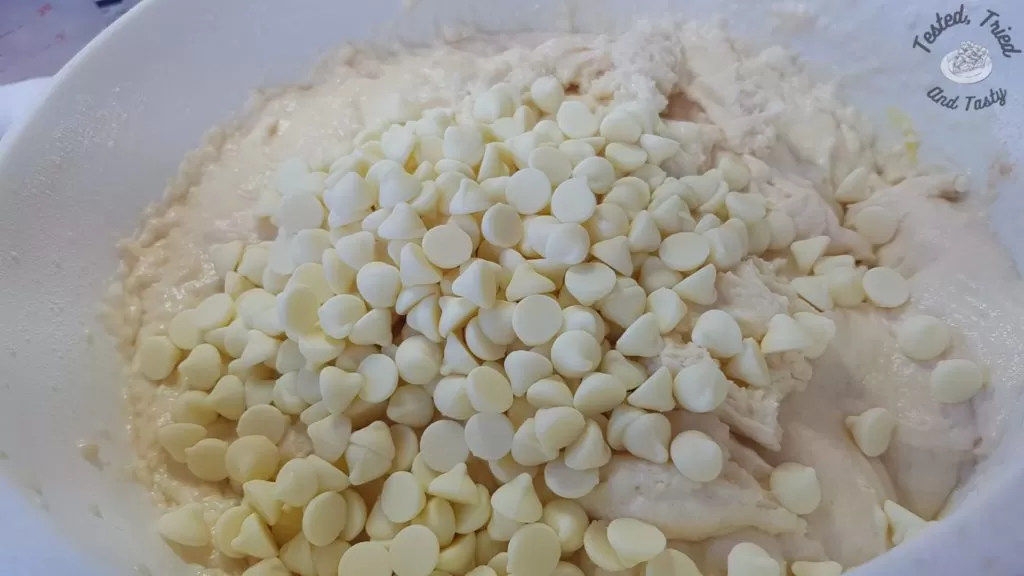 White chocolate chips added to the muffin batter in a white bowl.