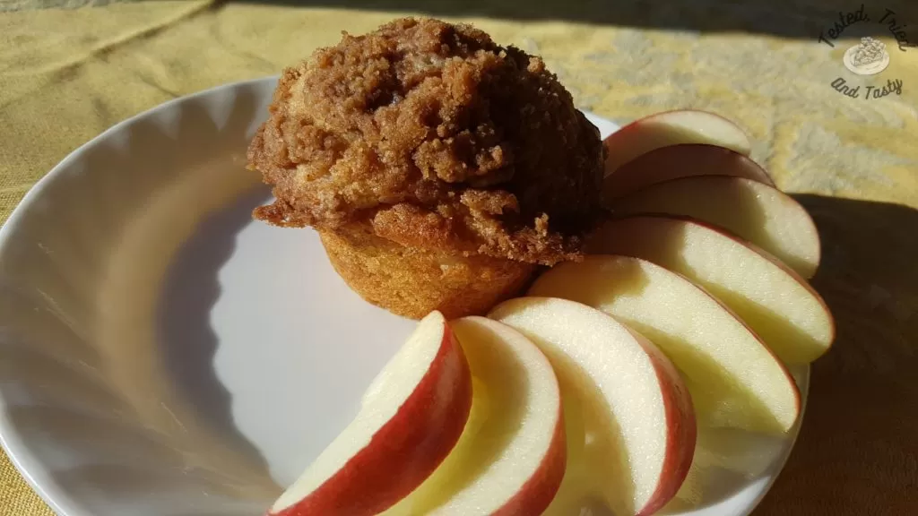Apple streusel muffin with apple slices on a white plate.