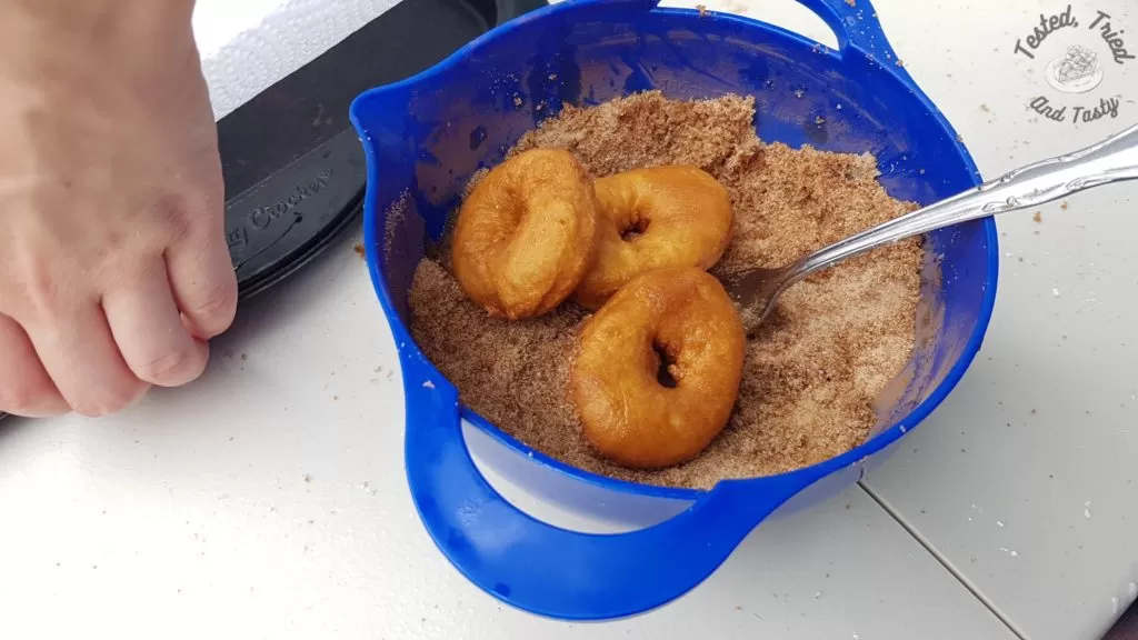 Coating the mini donuts with cinnamon sugar.