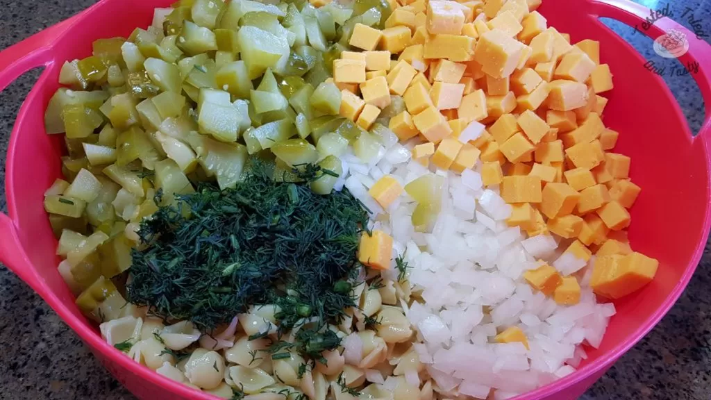 Ingredients for dill pickle pasta salad in a red bowl.
