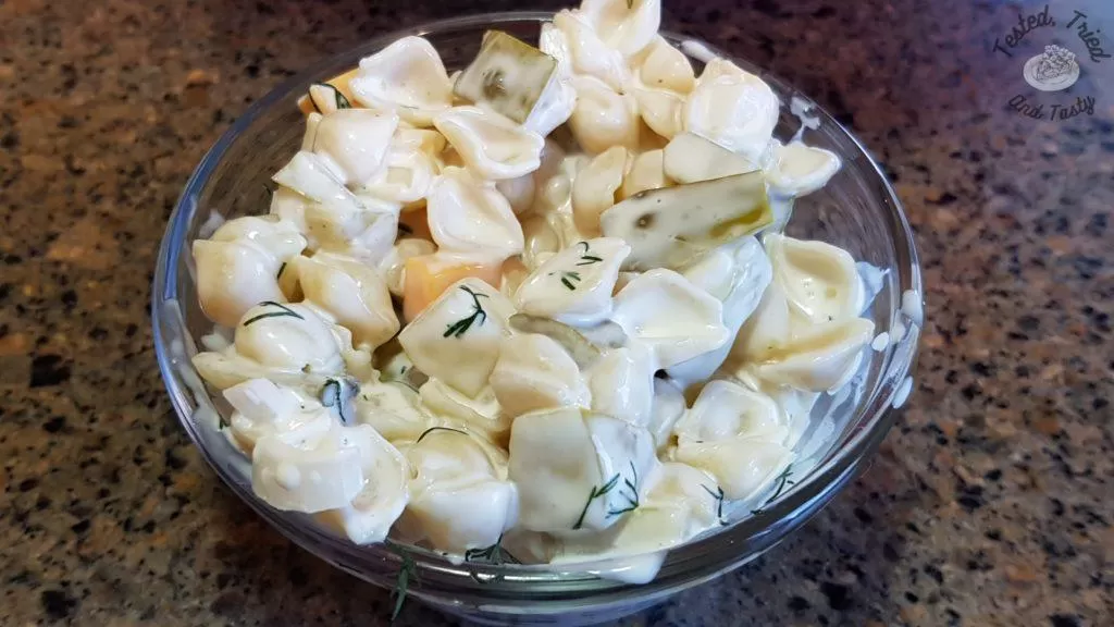 Dill pickle pasta salad in a glas bowl on a marble countertop.