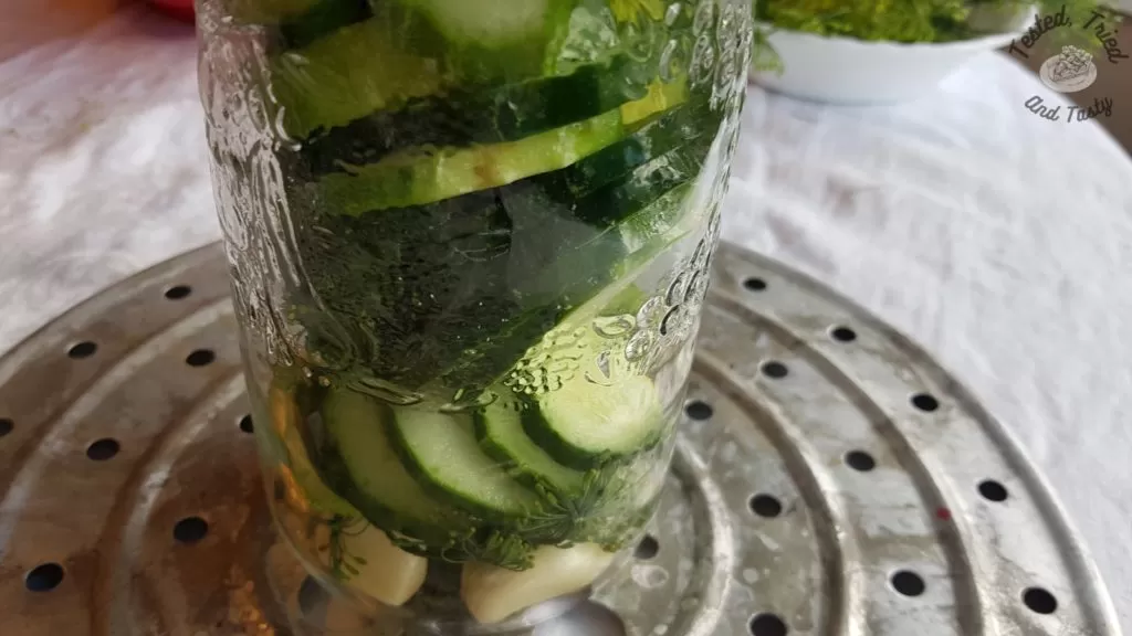 Quart jar filled with garlic, dill heads, and sliced cucumbers.