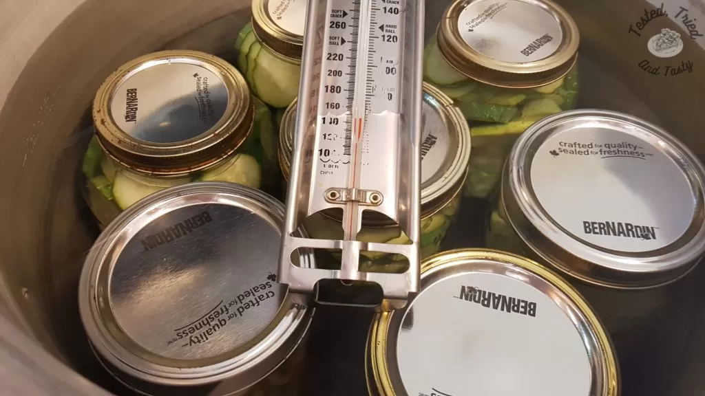 A candy thermometer on top of jars of pickles.
