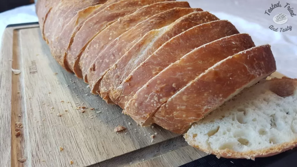 Sourdough french bread sliced on a wooden cutting board.