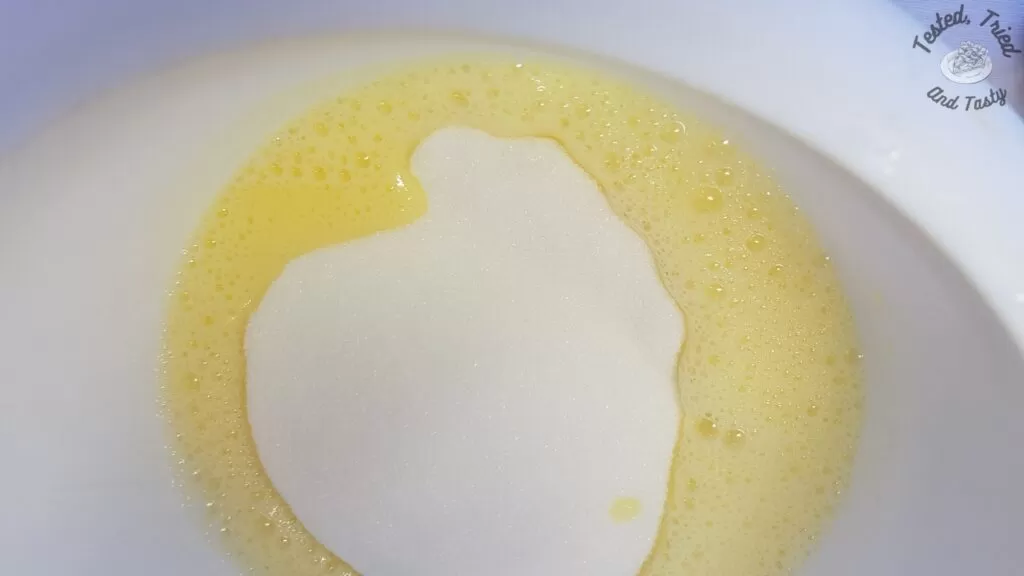 Granulated sugar added to beaten eggs in a white bowl.