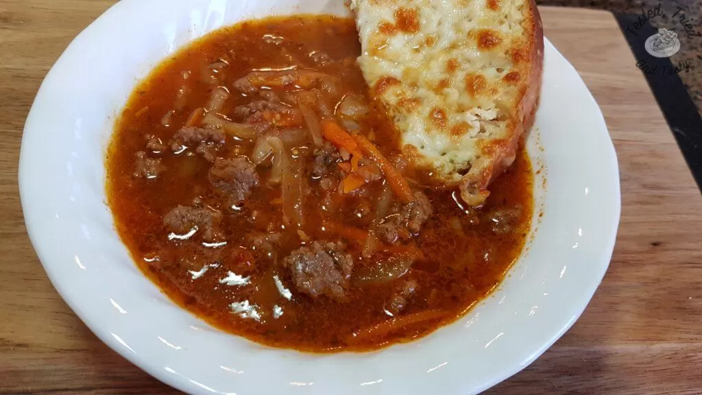 Homemade hamburger soup with homemade garlic bread in a white bowl.