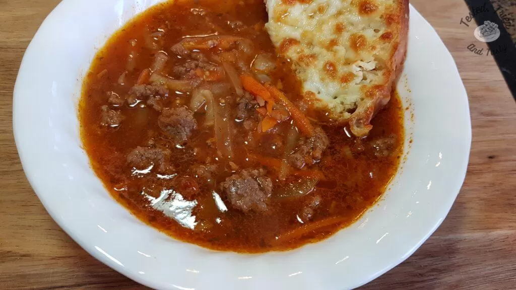 Ground beef soup with homemade garlic bread in a white bowl.