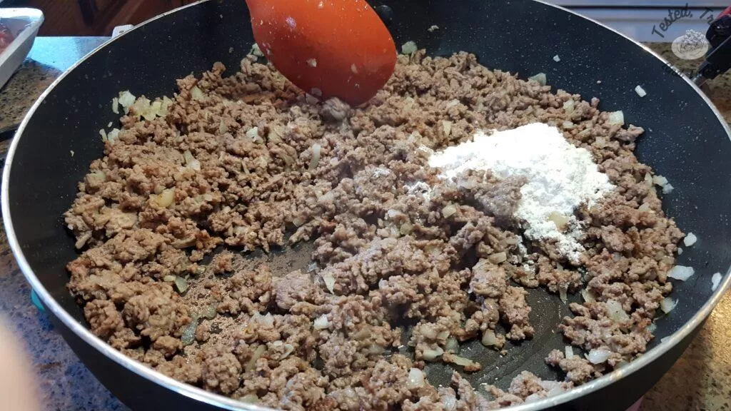 Adding flour to the ground beef in a large saucepan.