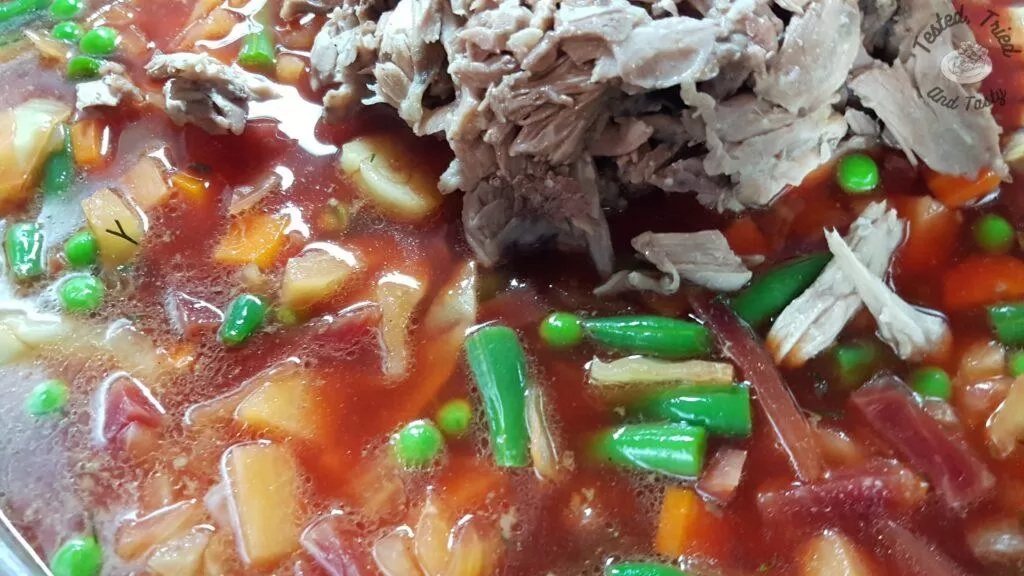 Adding pork to the cooked vegetables for beet borscht recipe.