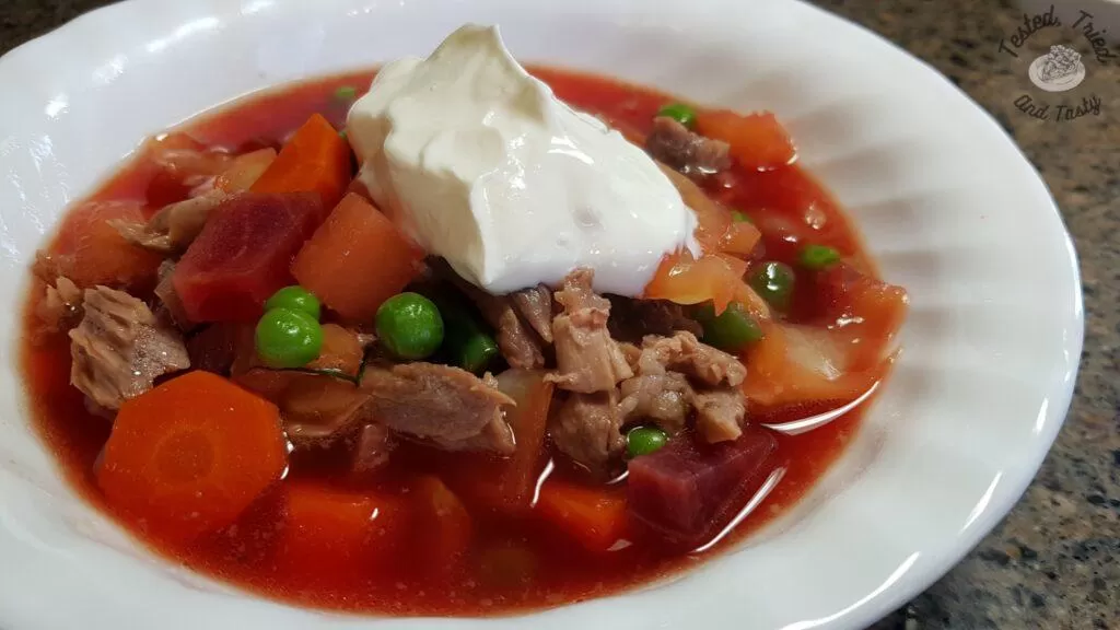 Beet borscht recipe in a white bowl, with a dollop of sour cream.