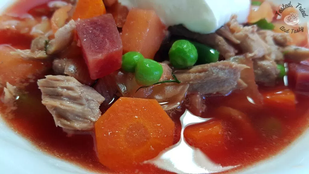 Beet borscht recipe in a white bowl, with a dollop of sour cream.