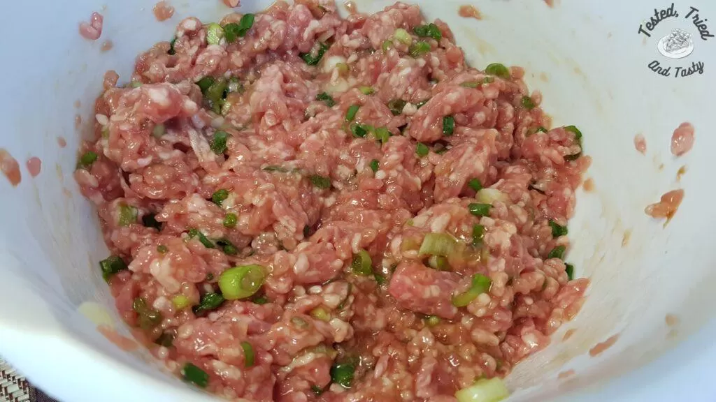 Filling of ground pork, egg, soy sauce, oyster sauce, sugar, and green onions mixed in a white bowl.