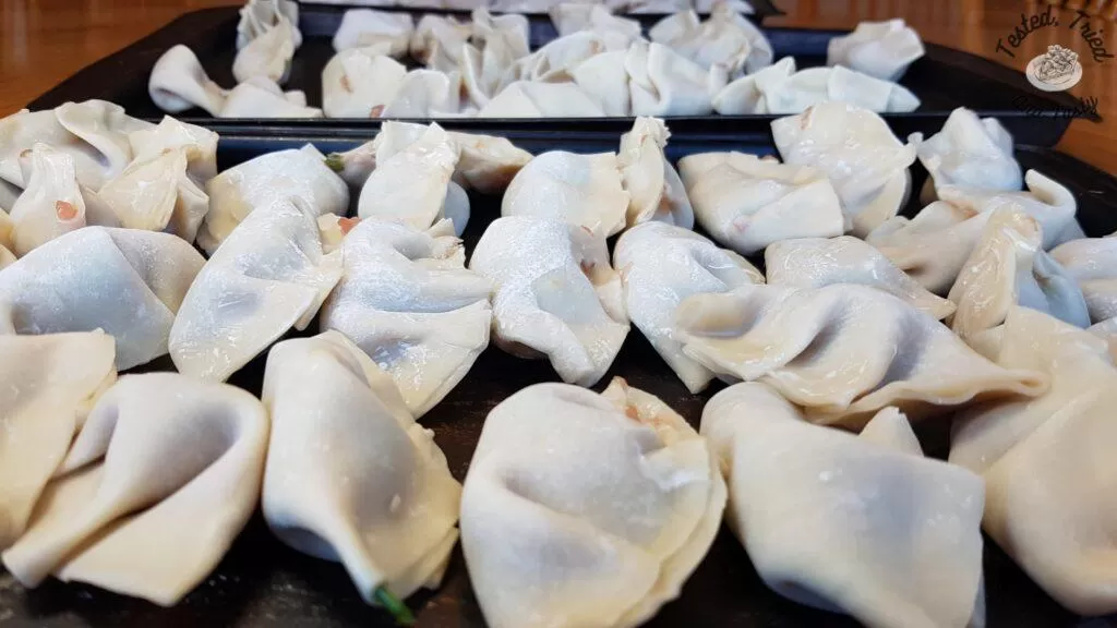 Homemade wontons on baking sheets ready to be frozen.