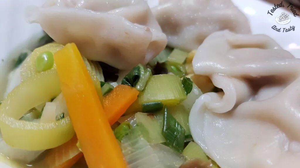 Wor wonton soup in a white soup bowl.