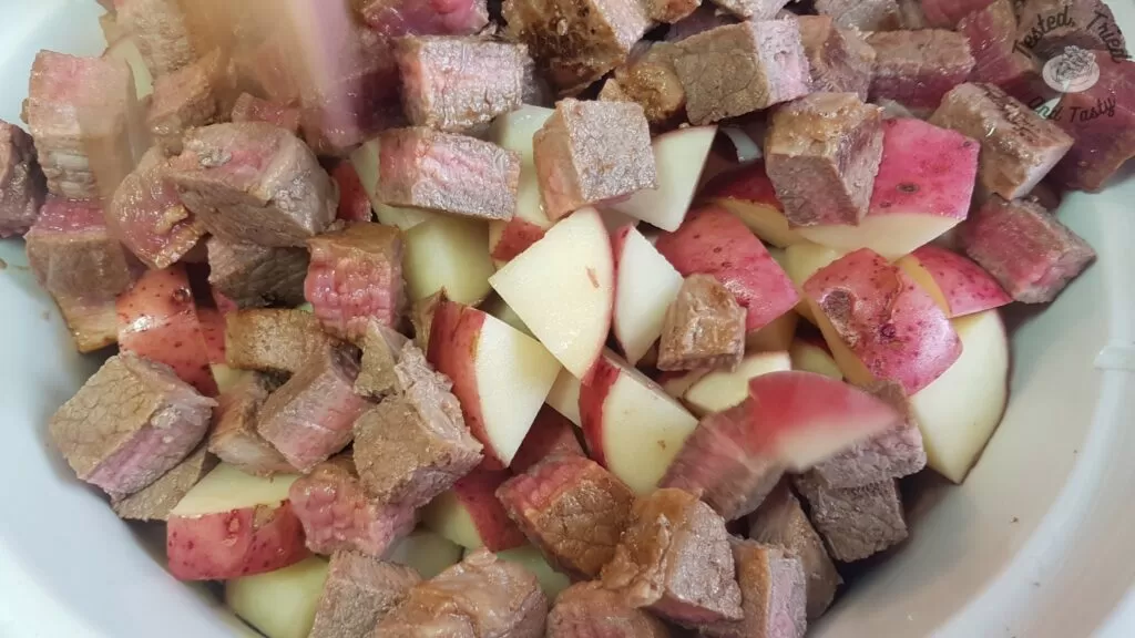 Adding the beef cubes to the crock pot for slow cooker beef stew.