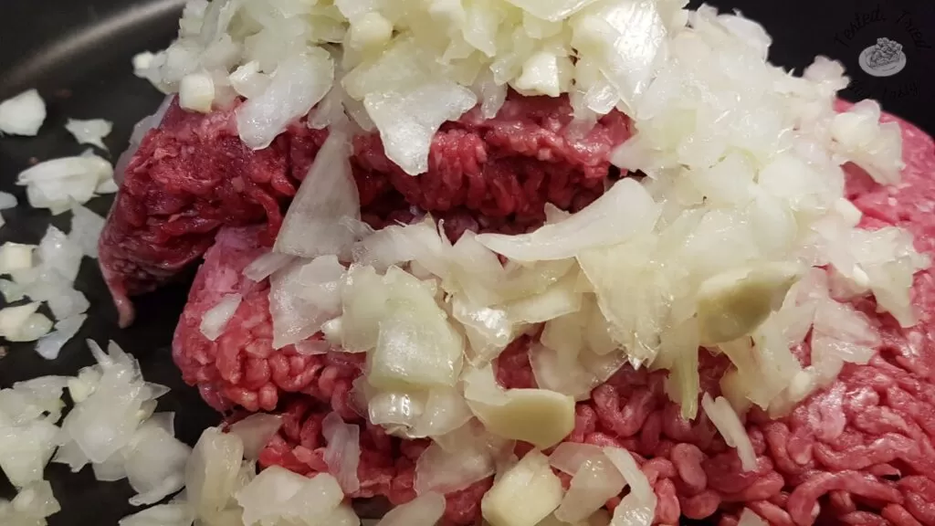 Ground beef and chopped onions in a large skillet.