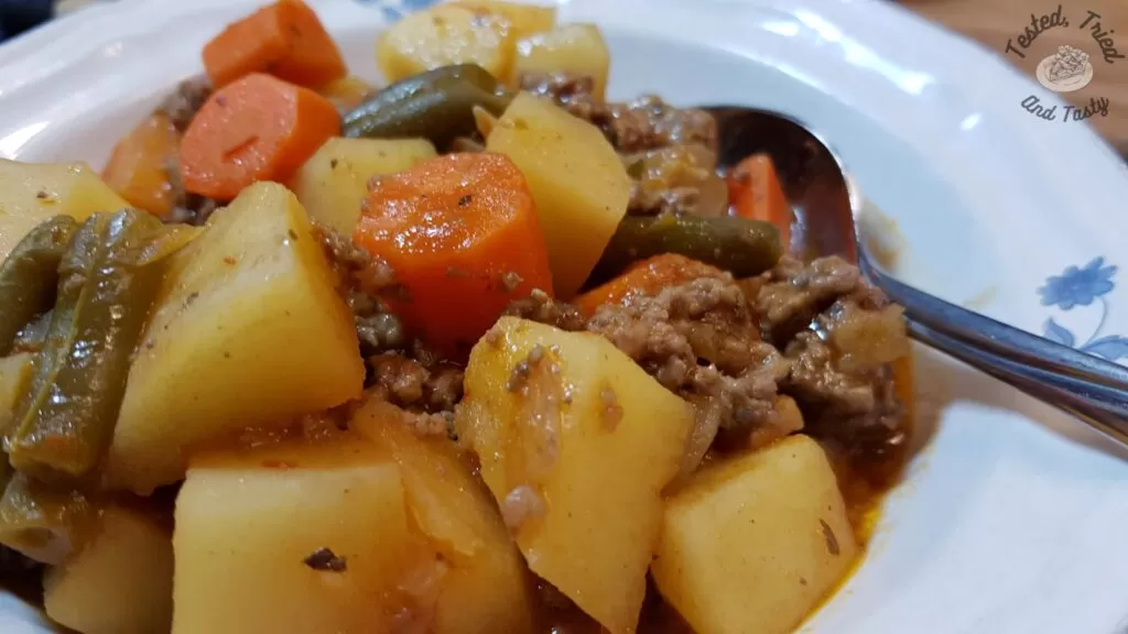 Stovetop hamburger stew in a soup dish with a spoon.
